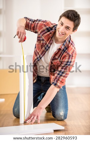 Happy handsome man measuring home furniture with measure tape. Repair concept.