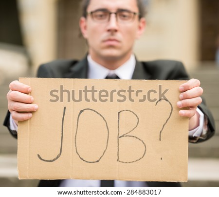 Man in suit sitting at stairs with sign in hands. Unemployed man looking for job.