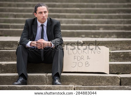 Man in suit sitting at stairs with sign. Unemployed man looking for job.