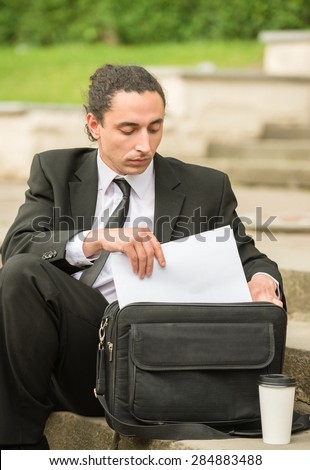 Man in suit sitting at lawn with briefcase.