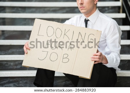 Close-up of man in suit sitting at stairs with sign in hands. Unemployed man looking for job.