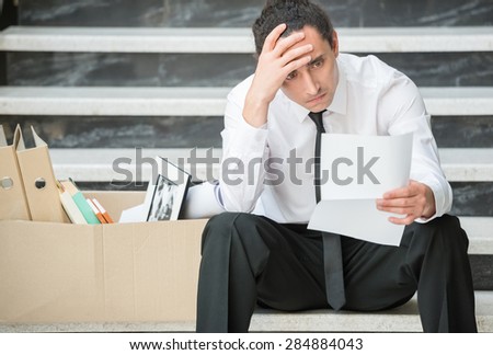Fired frustrated man in suit sitting at stairs in office.