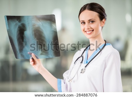 Young smiling female doctor with stethoscope looking at X-ray at doctor\'s office.
