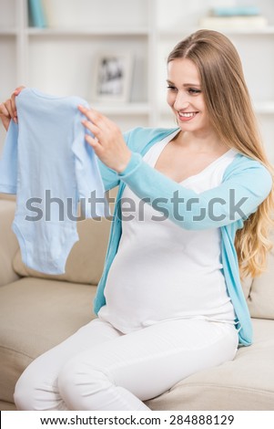 Beautiful pregnant woman sitting at sofa and holding creepers.