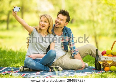 Young beautiful couple dressed casual having picnic in park and making selfie.