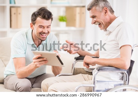 Smiling handsome man taking care about his eldery father in wheelchair.