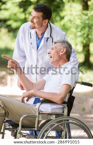 Male nurse talking with senior patient in wheelchair in garden near hospital. Side view.