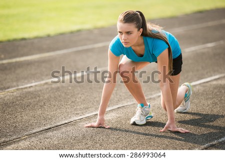 Attractive sporty girl ready to run sprint. Female athlete in powerful starting line pose.