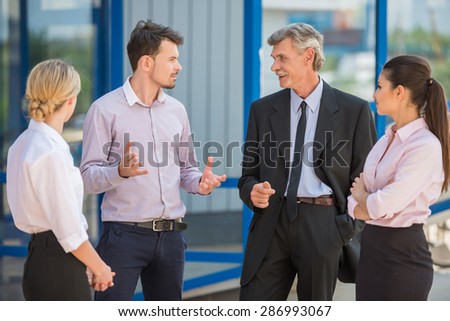 Group of successful people in suits standing in front of office and discussing business strategy.