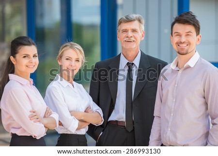 Group of successful people in suits standing in front of office and smiling  at camera.