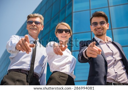 Three successful business people in suits posing to camera outdoors. Office background.
