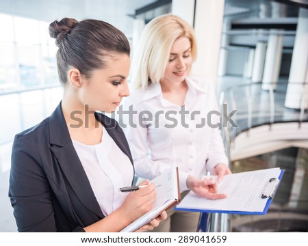 Two beautiful female business partners dressed formal discuss project at office.