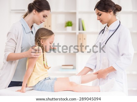 Pediatrician doctor bandaging child\'s leg. Mother holding baby in her hands.
