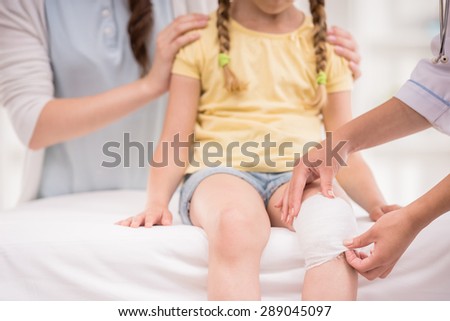 Pediatrician doctor bandaging child\'s leg. Mother holding baby in her hands. Close-up.