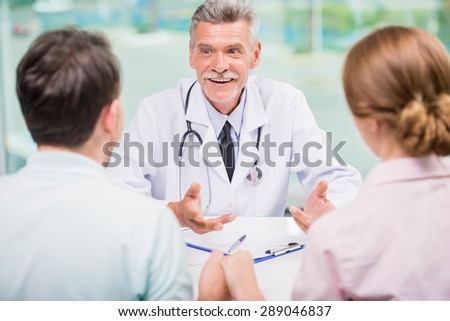 Cheerful doctor talking with family couple at clinic.