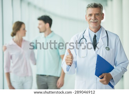 Cheerful doctor standing at clinic and smiling at camera with patients on background.
