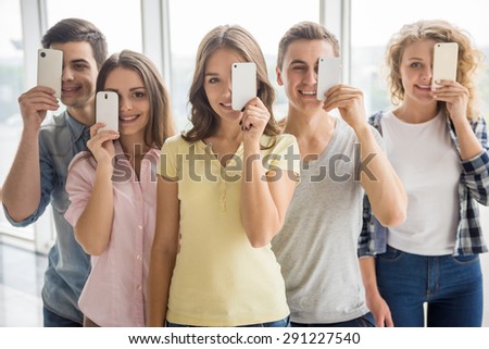 Friendship, technology and internet concept - smiling friends standing in line with their phones.