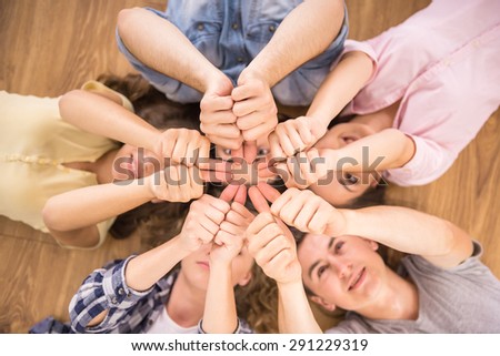 Education and happiness concept - group of young smiling people lying down on floor in circle and showing thumbs up.