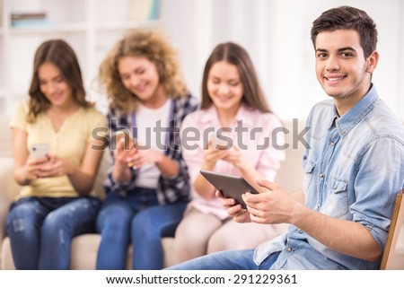 Group of young positive friends sitting at sofa and using their phones. Education concept. Front view.