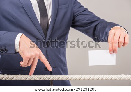 Close-up of business man\'s hand walking with fingers on rope and holding business card in another hand.