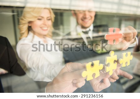 Group of confident business people trying to connect small pieces of puzzle at office.