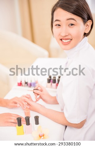 Pretty asian manicurist applying nail polish to client. Hands care concept.