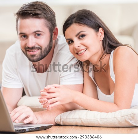 Young beautiful couple lying on the floor at home and using laptop.