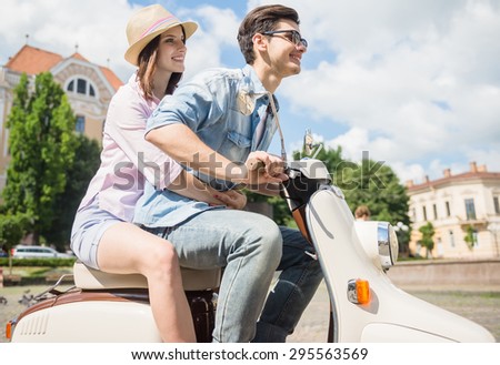 Beautiful young couple riding scooter together, woman hugging her boyfriend. Side view.