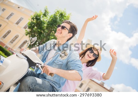 Young stylish couple riding scooter together,  happy woman raising arms and smiling. Happy weekend.