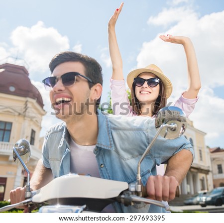 Beautiful happy couple riding scooter and having fun, woman raising hands and smiling.