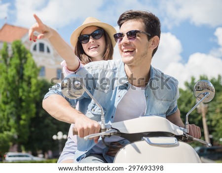 Beautiful young couple riding scooter together, happy woman pointing away.