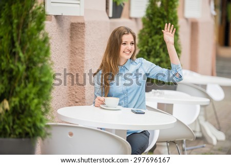 Happy young woman sitting at urban cafe in summer and asking for waiter.
