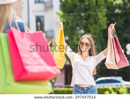 Cheerful young woman in sunglasses with shopping bags meeting her friend at the street.