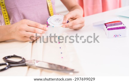 Female fashion designer sitting in her office, working in progress at the tailor table, close-up.