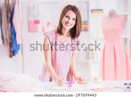 Beautiful young woman with measuring tape on shoulders looking at camera and  drawing.