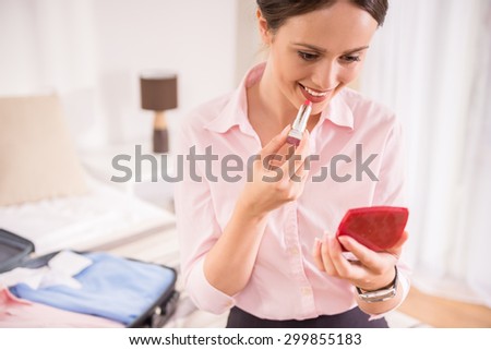 Beautiful woman holding lipstick, looking in the mirror at the hotel room.