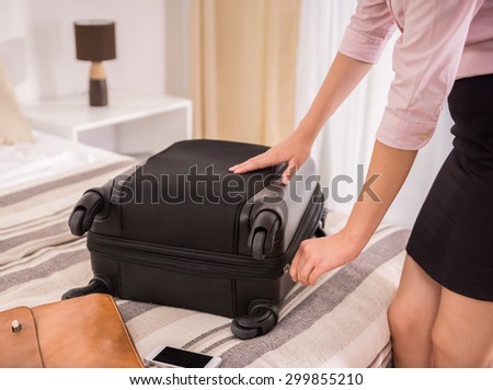 Young business woman packing her suitcase on bed at the hotel room. Close-up.