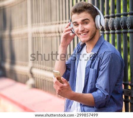 Handsome man listen to music with headphones while sitting near the fence outdoors.