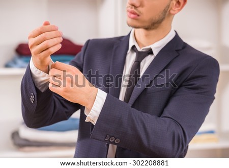 Young handsome man in suit buttoning shirt sleeve. Close-up.