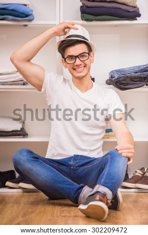 Handsome man in glasses and hat sitting at the dressing room and smiling at camera.