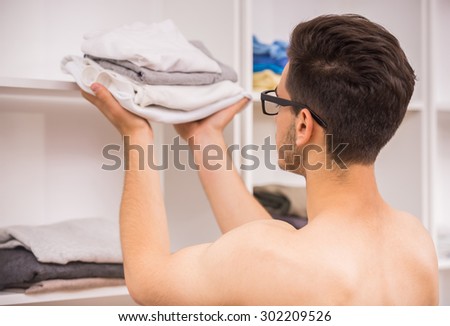 Young man in glasses taking clothes from the wardrobe. Back view.