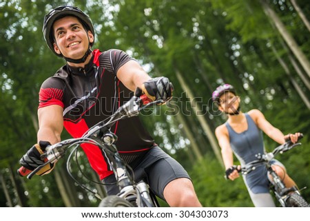 Young sporty couple riding on bicycles at the forest road. Man in front of woman.