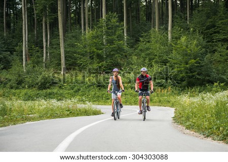 Young sporty couple riding on mountain bicycle on the forest road. Front view.