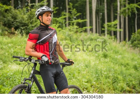 Handsome man standing with his bicycle near forest and looking away.