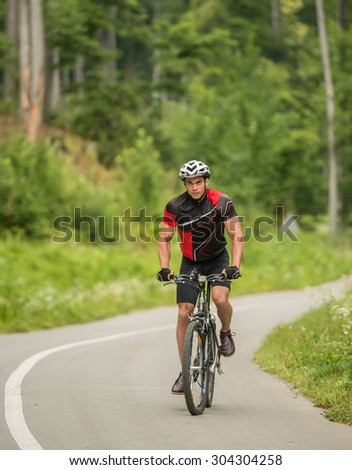 Young man in helmet riding on mountain bicycle on the forest road.