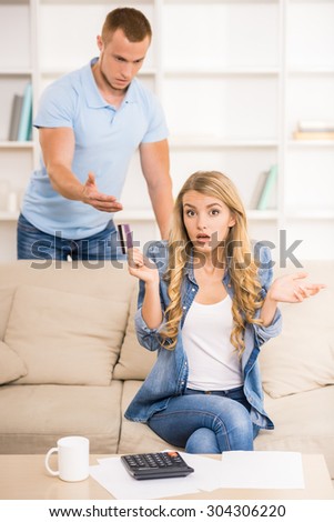 Woman calculating great expenses while her husband holding credit card and arguing with her.