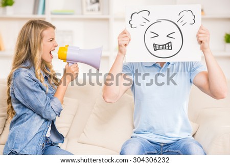 Wife shouting on her husband with mouthpiece while he holding image of angry face.