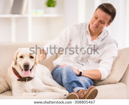 Young smiling man is playing with his dog sitting on sofa.