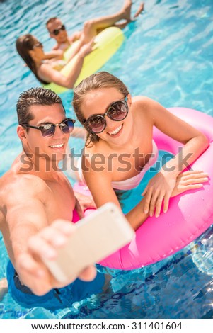 Happy young couple are making selfie while having fun in pool.