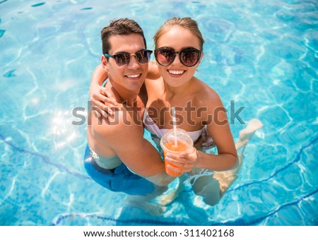 Top view of young couple relaxing in resort swimming pool and drinking cocktails.